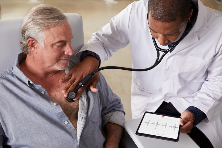 Dr looking at PCG on tablet while listening to heart sounds on patient's chest